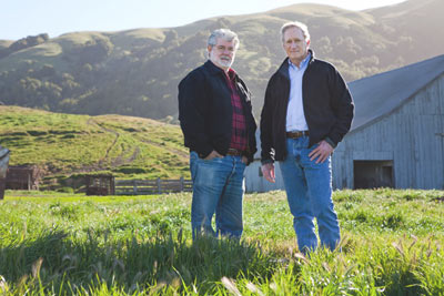 George Lucas and former MALT Executive Director Bob Berner standing in front of a barn in a field of green grass and rolling hills