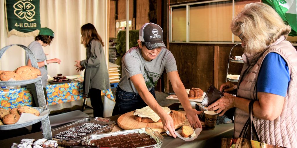 Denise Rocco Zilber, in a MALT hat, is working the Olema 4-H booth at the Point Reyes Farmers' Market, serving up freshly-based pastries at an event in Marin. 