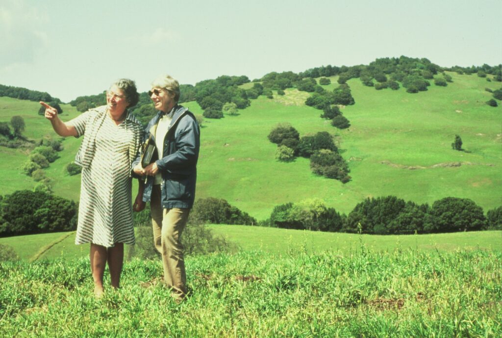Ellen Straus and Phyllis Faber standing on a lush green hillside in Marin in the earlier days of MALT's history.