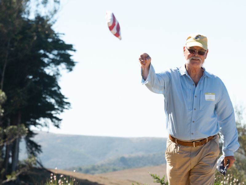 Larry Petersen playing corn hole, tossing a beanbag through the air at a ranch in Marin.