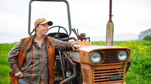 Moira Kuhn of Marin Roots Farm stands beside a weathered Kubota tractor in a field at the MALT-protected Volpi Ranch in Marin County.